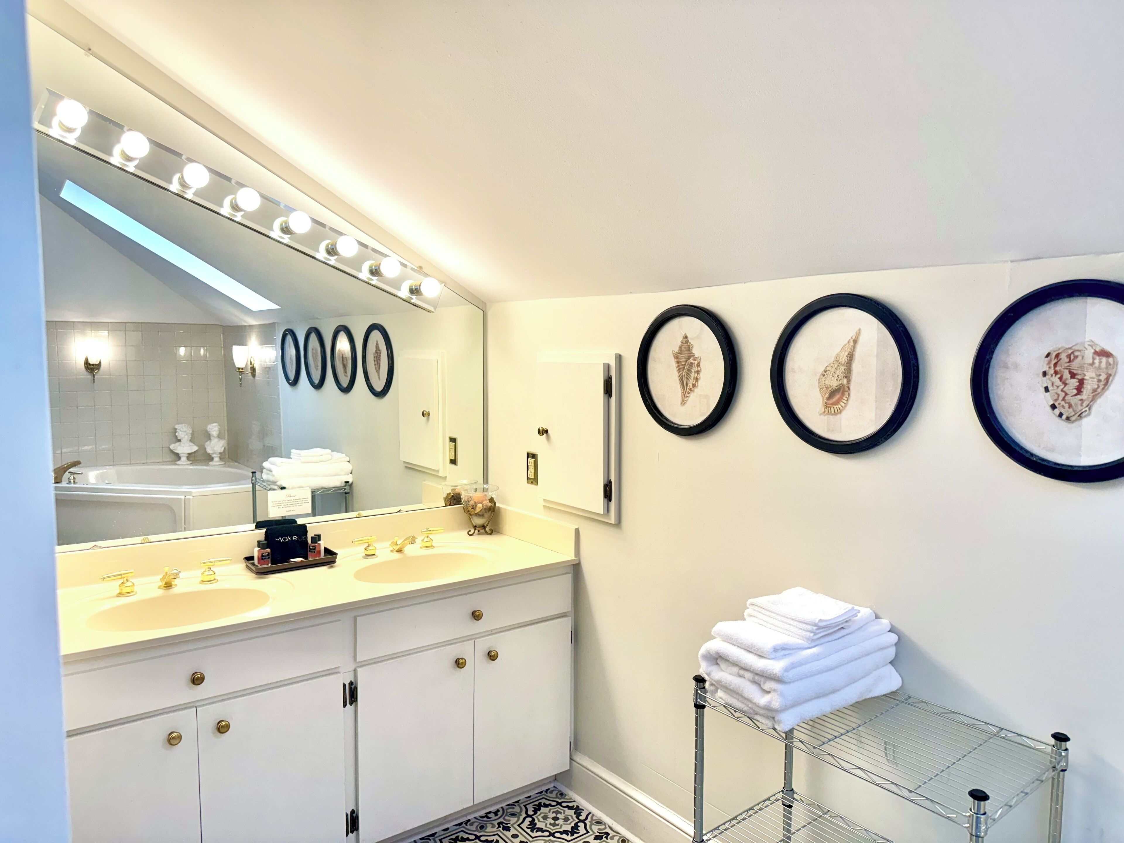A modern bathroom with a large mirror, dual sinks, and a vanity with gold handles.
