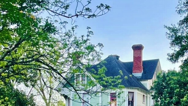 A large, two-story house with a prominent red chimney, surrounded by well-manicured hedges and a fountain. - Peacock Place (Eastman)