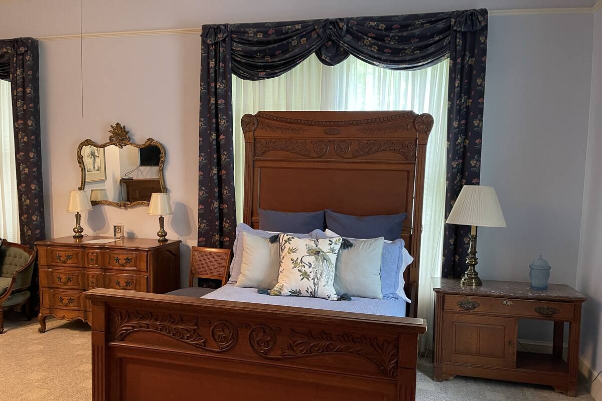 Um quarto tradicional com uma cama de dossel, um aparador de madeira, uma mesinha de cabeceira e um espelho.