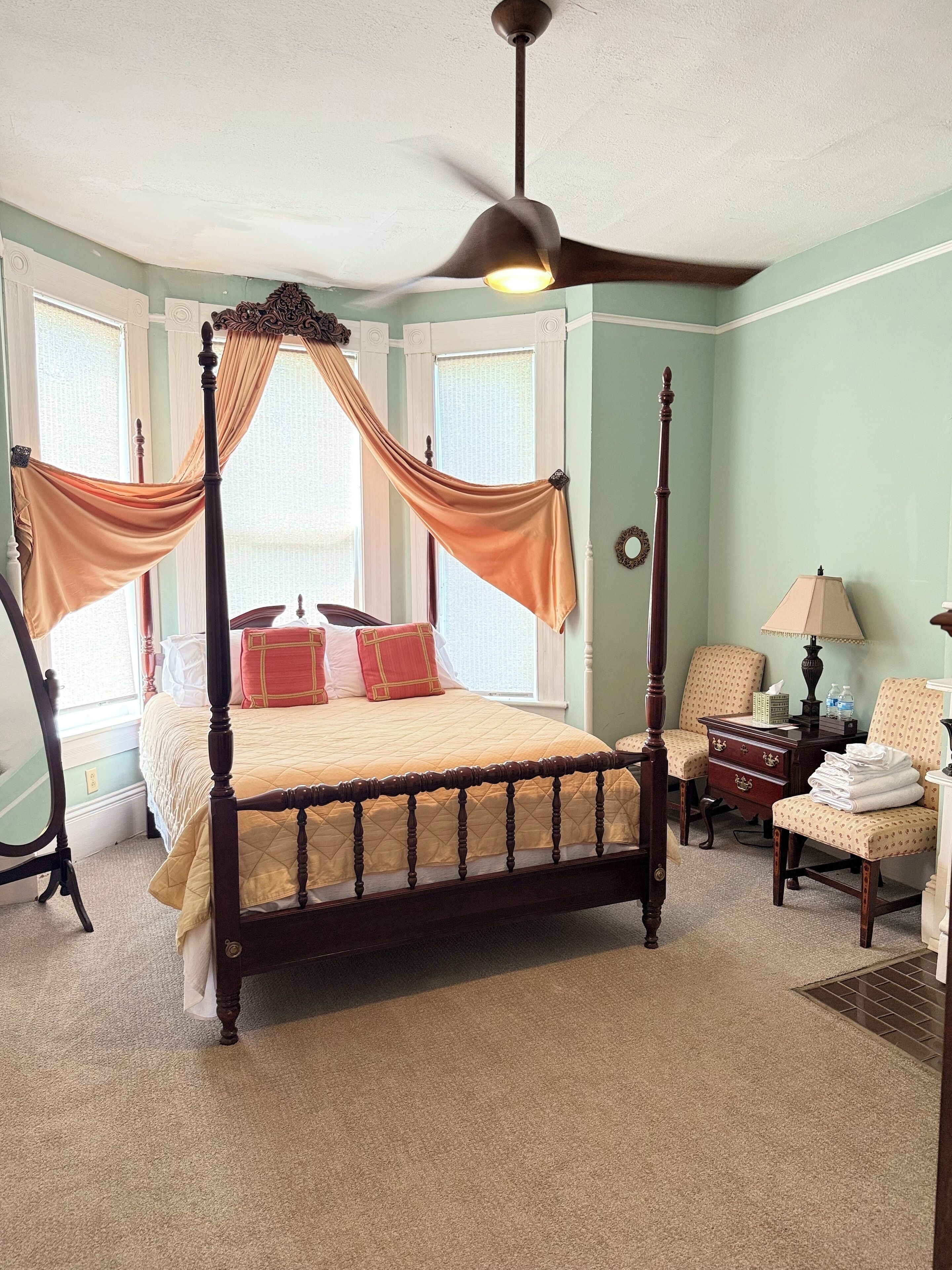 A four-poster bed with a canopy, a bedside table with a lamp, and a chair.
