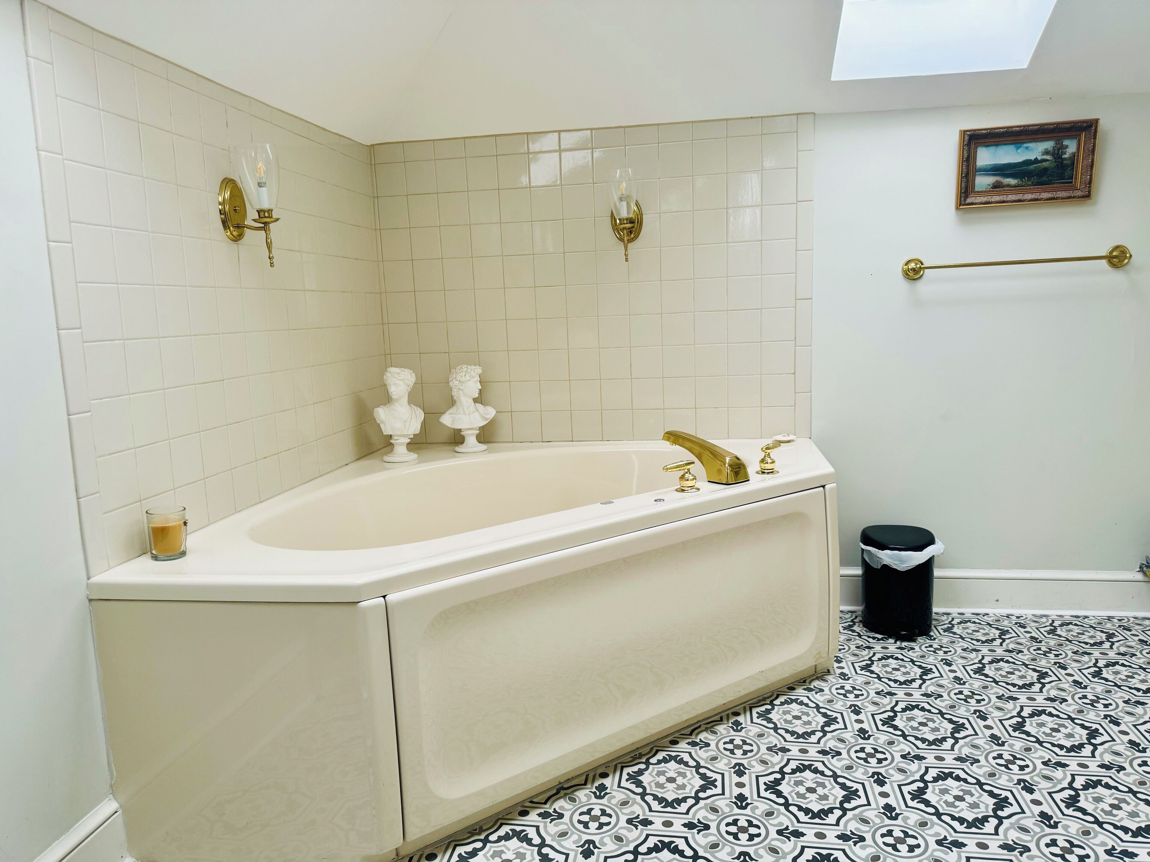 Une salle de bain avec une baignoire, deux appliques murales, un porte-serviettes et un carrelage décoratif.