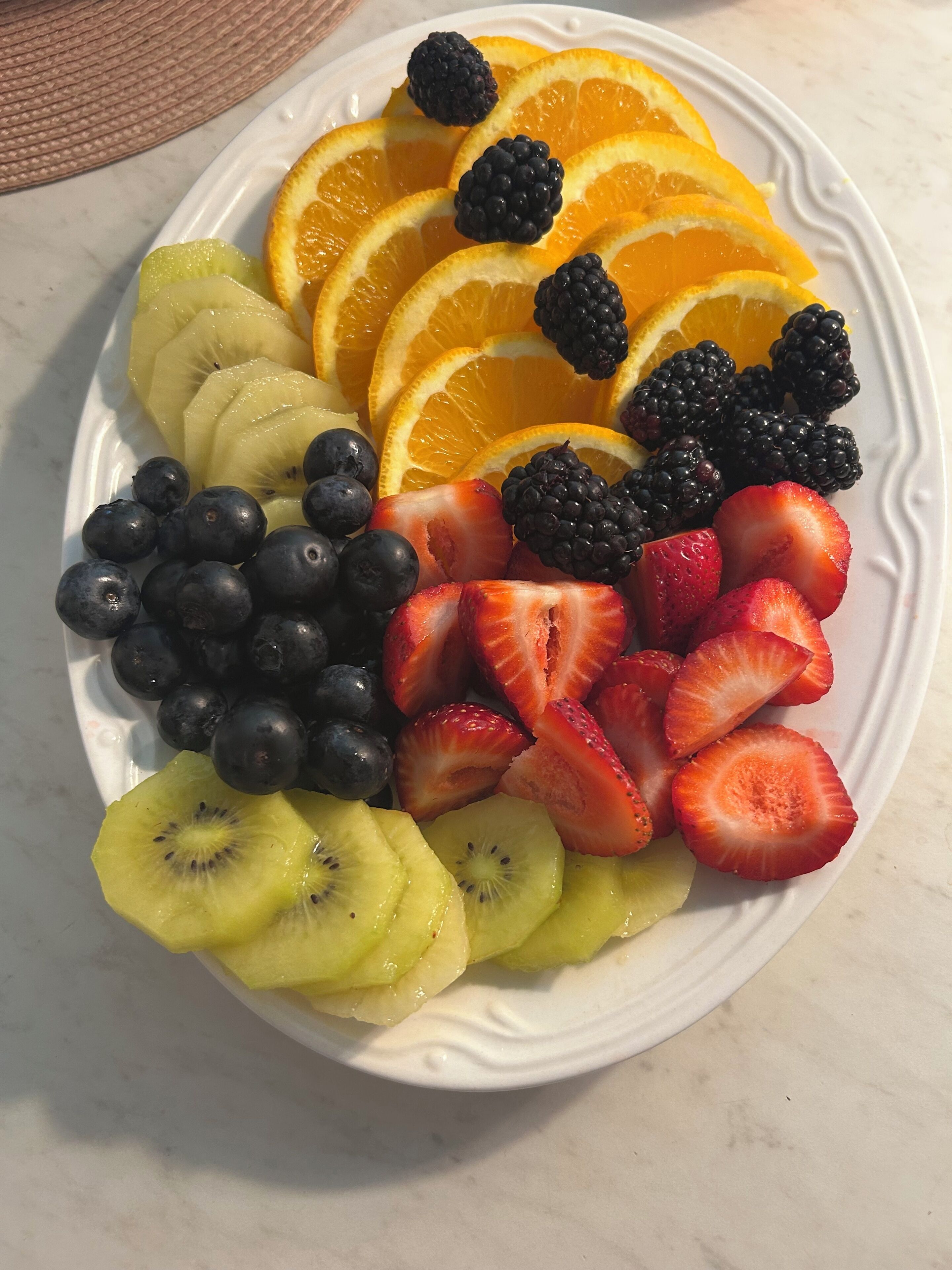 Um prato com frutas variadas, incluindo kiwi, mirtilos, morangos, framboesas e fatias de laranja.