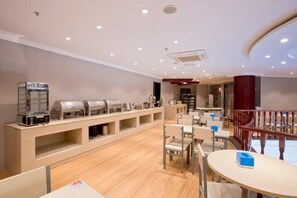 A hotel dining area with a buffet setup, seating arrangements, and a staircase.