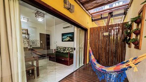 A room with a hammock, wooden flooring, a glass door leading to another room, and a painting on the wall. - Conchas do Mar Residence (Itacaré)