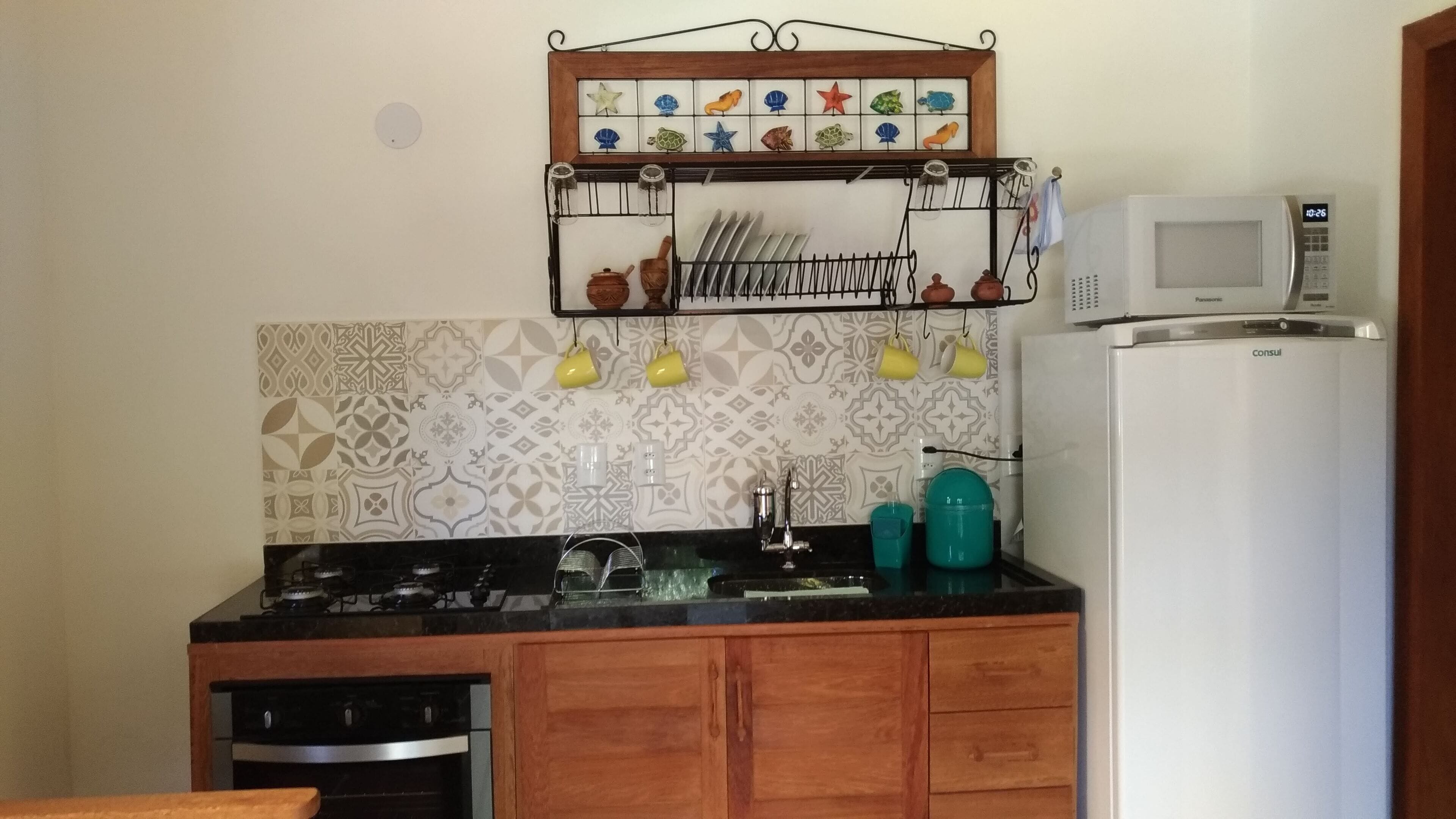 A compact kitchen with a stove, sink, and a microwave. There is a dish rack above the sink and a decorative tile backsplash.