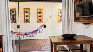 A room with a wooden table, a hammock, and a television on the wall. - Conchas do Mar Residence (Itacaré)