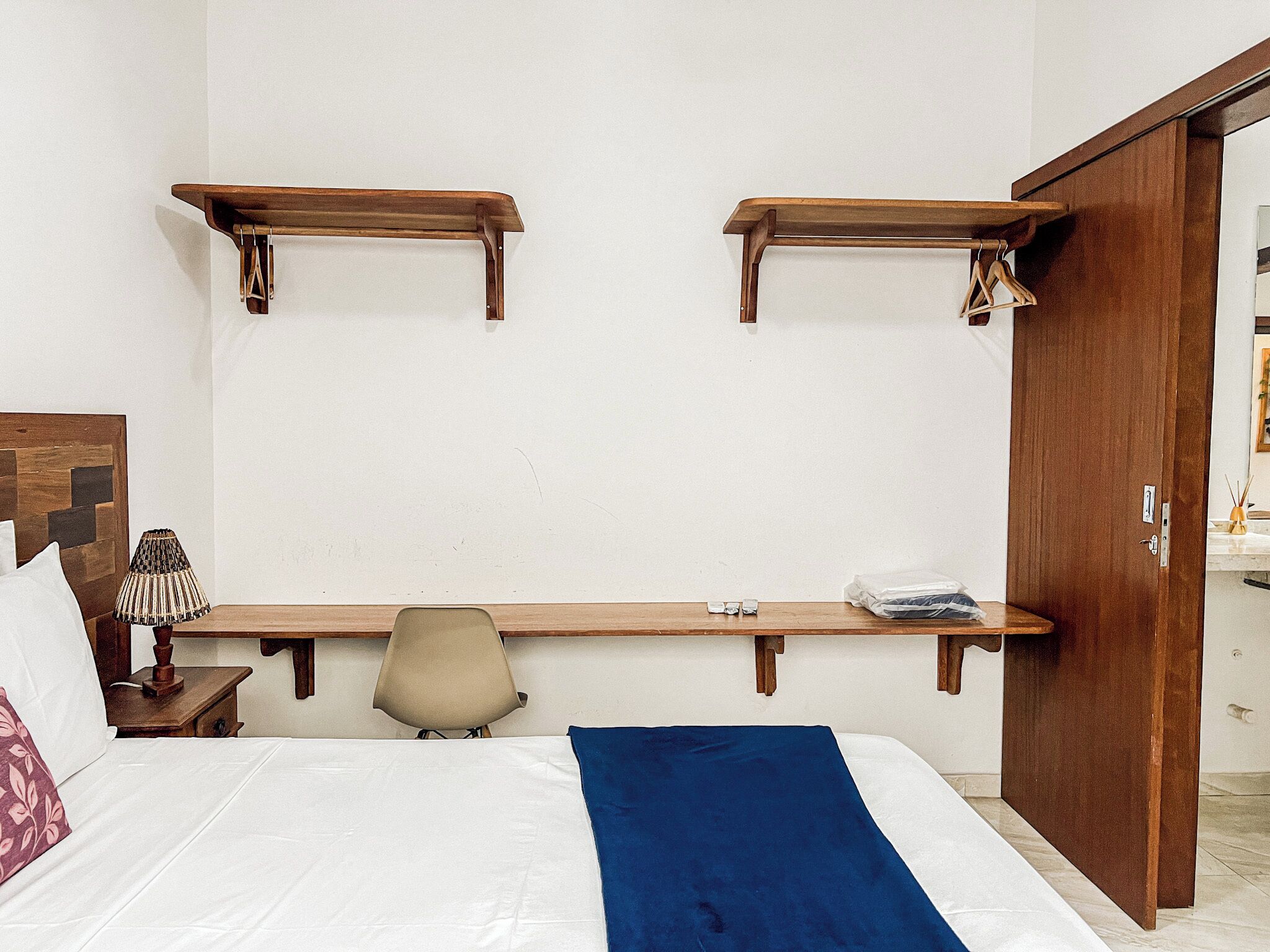Un dormitorio con una cama, una silla, un escritorio y dos estanterías de madera.