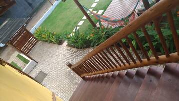 A wooden staircase leading to a balcony with a view of a garden and a hammock.