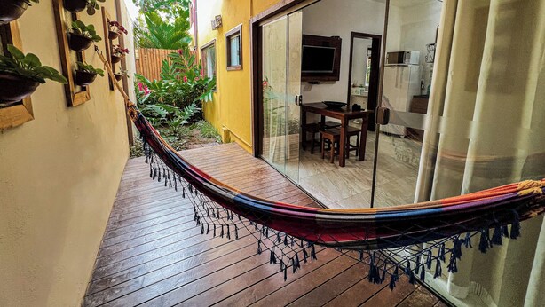 A hammock on a wooden deck, a sliding glass door leading to a dining area, and potted plants on the wall. - Conchas do Mar Residence (Itacaré)