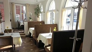 A restaurant with high tables and benches, potted plants, and a view through large windows.