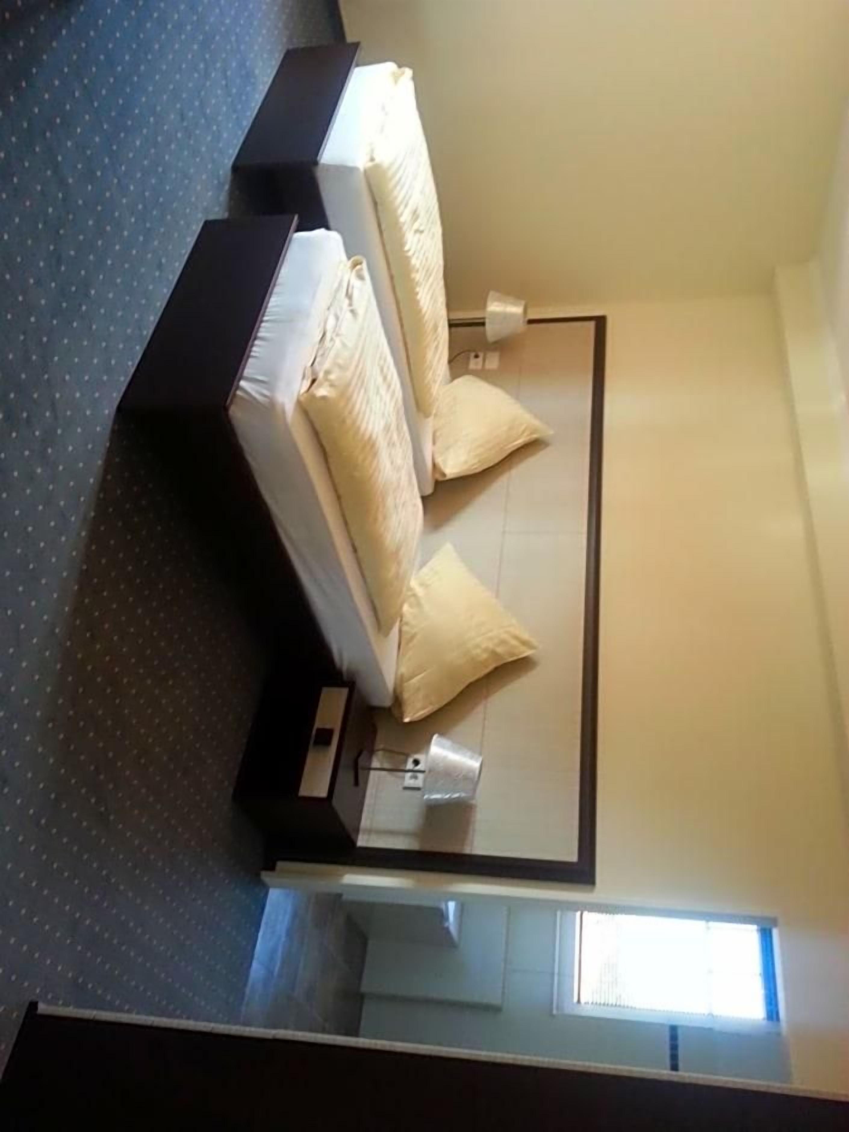 A hotel room with a bed, a nightstand, a mirror, and a window.