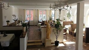 A spacious dining area with a central statue, multiple tables, and potted plants.
