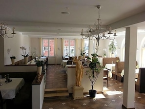A spacious dining area with a central statue, multiple tables, and potted plants.