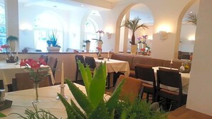 A restaurant interior with tables, chairs, potted plants, and a warm ambiance.