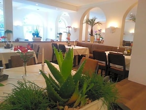 A restaurant interior with tables, chairs, potted plants, and a warm ambiance.