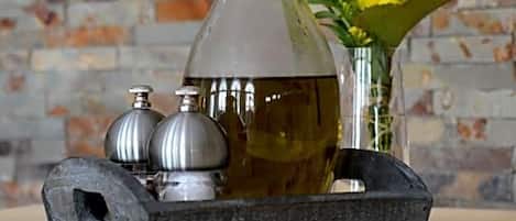Une bouteille en verre transparent fermée par un bouchon en liège, un plateau en métal et deux salières et poivrières en métal.