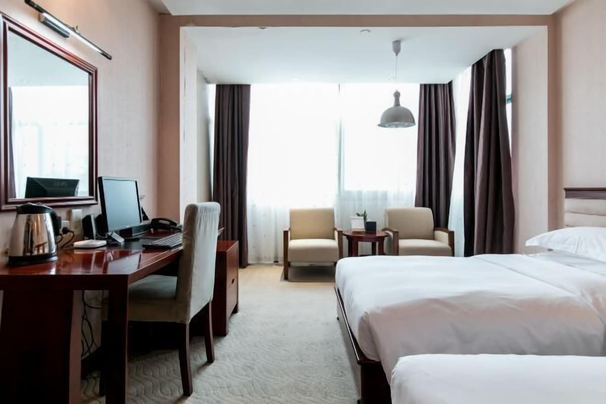Quarto de hotel com cama, escrivaninha com computador, cadeira e mesa pequena.