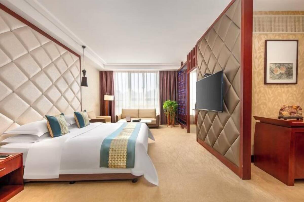 A hotel room with a large bed, a TV, a desk, and a window.