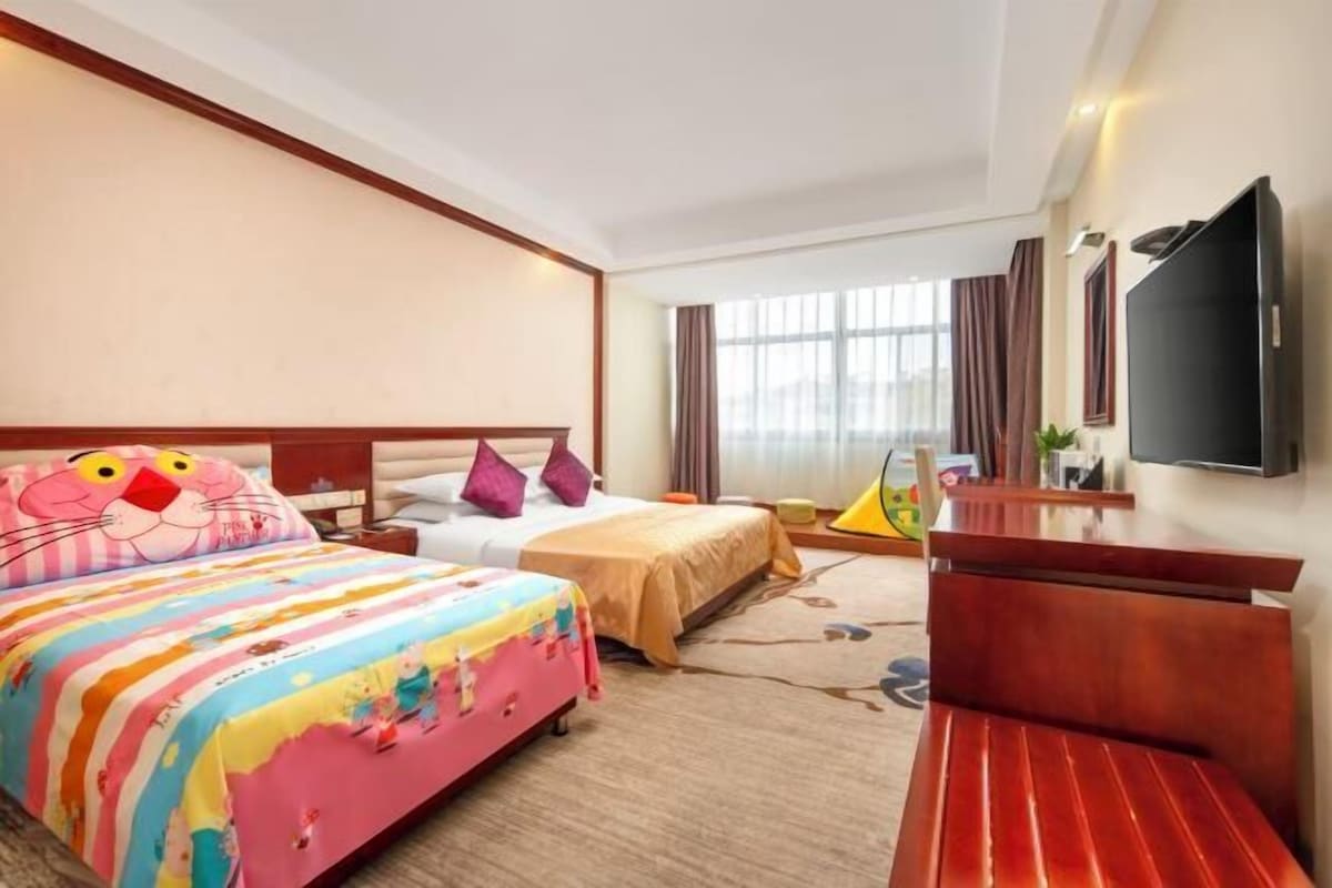 Quarto de hotel com uma cama grande, televisão, escrivaninha e janela com cortinas.