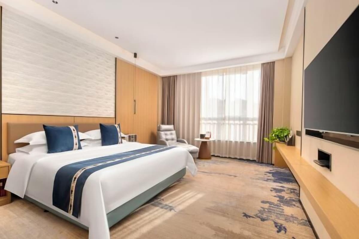 Quarto de hotel com uma cama grande, televisão, escrivaninha e janela com cortinas.