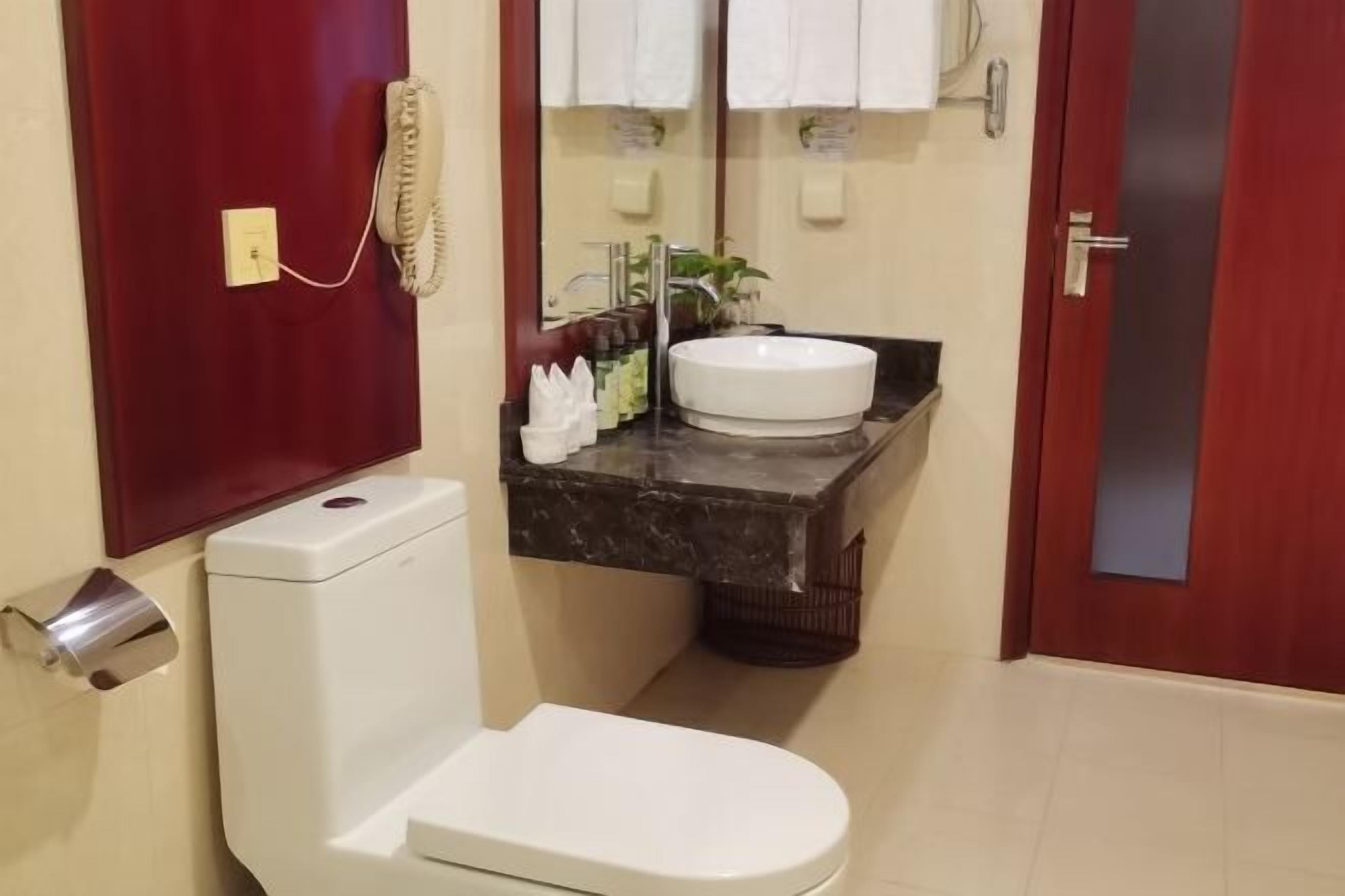 A bathroom with a white toilet, a sink with a marble countertop, a telephone, and a mirror above the sink.