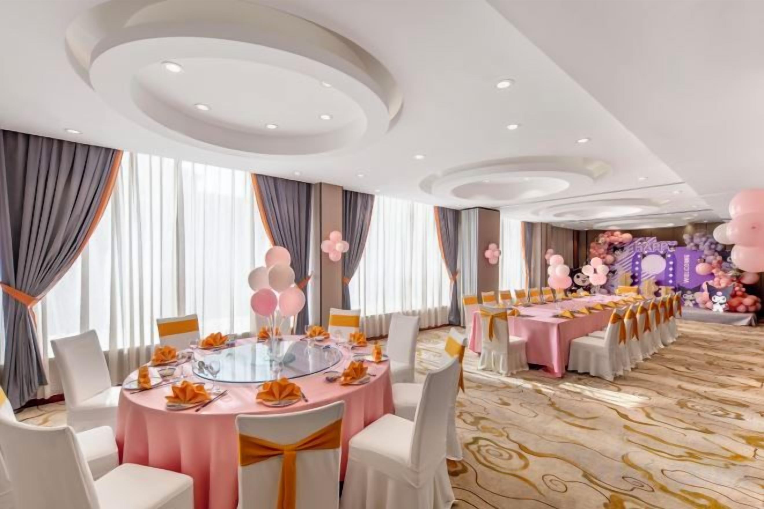 Un salón de banquetes con mesas redondas, sillas y un escenario decorado con flores.
