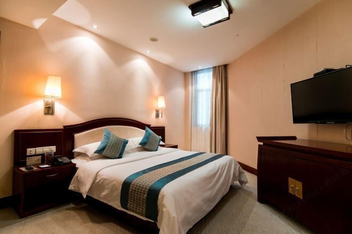 Quarto de hotel com uma cama grande, duas luminárias de cabeceira, uma televisão de tela plana e um aparador de madeira.