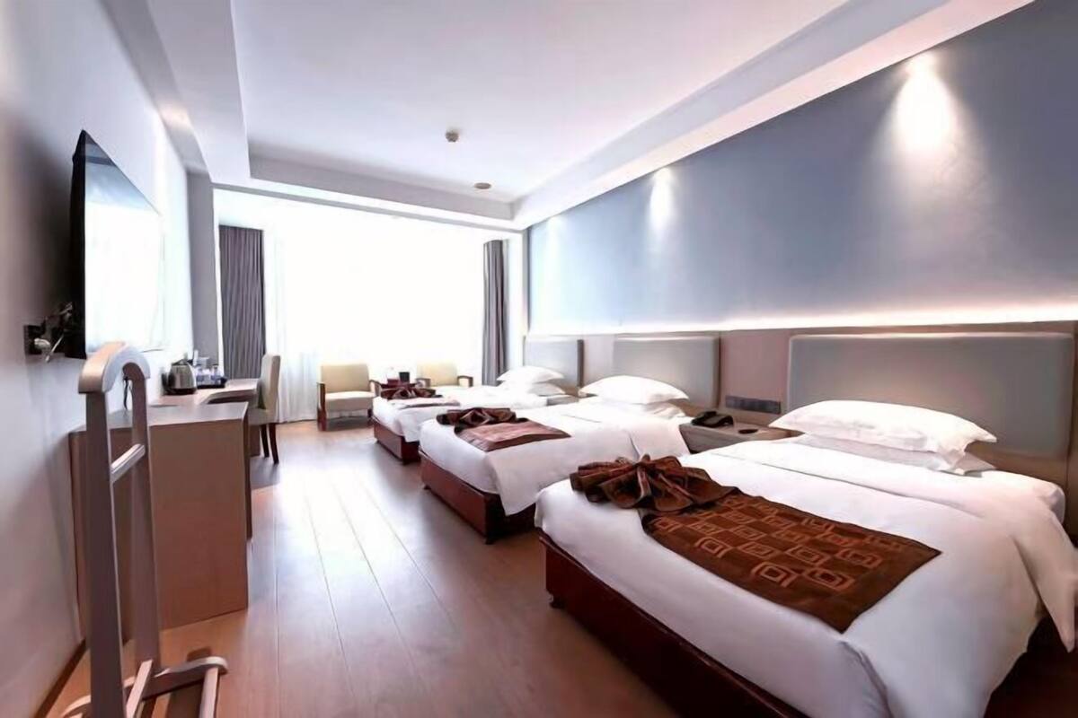 A hotel room with three beds, a desk, and a large window.