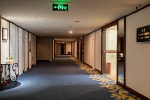 Un pasillo de hotel con piso alfombrado, un cartel de indicaciones y una puerta con números de habitación.