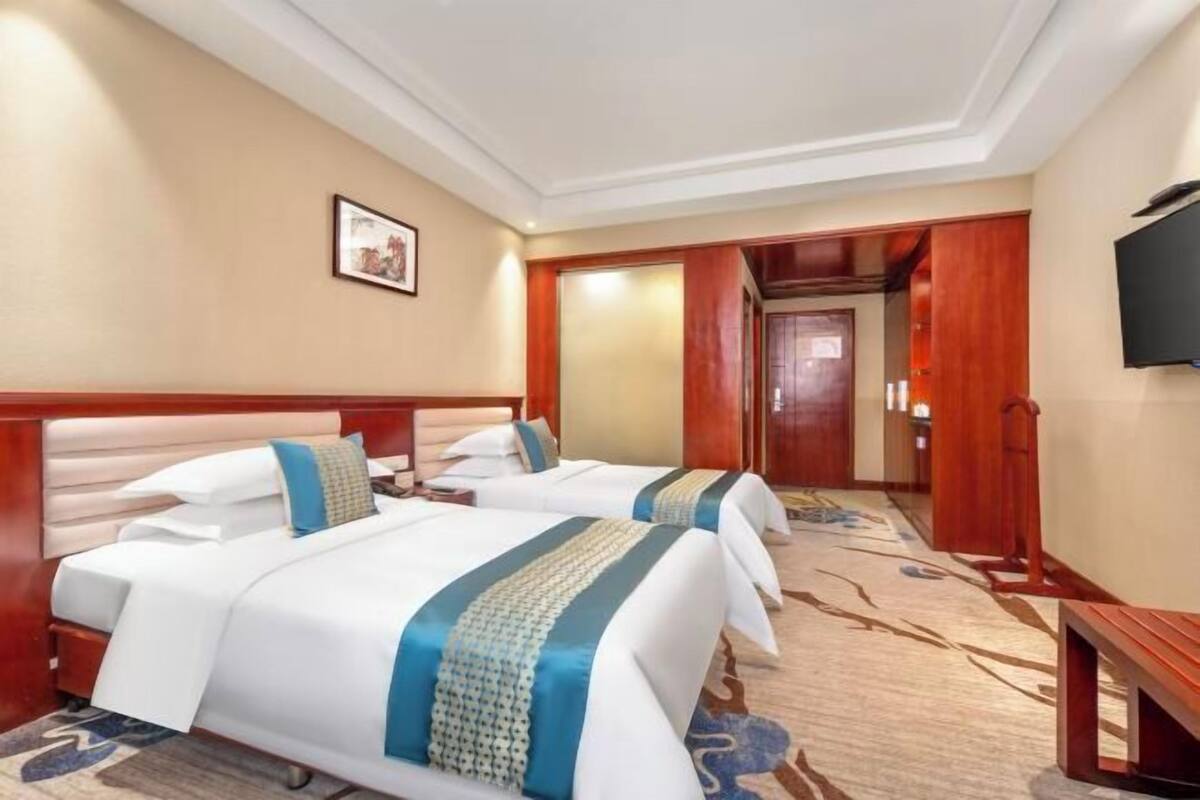 A hotel room with two beds, a television, and a carpeted floor.