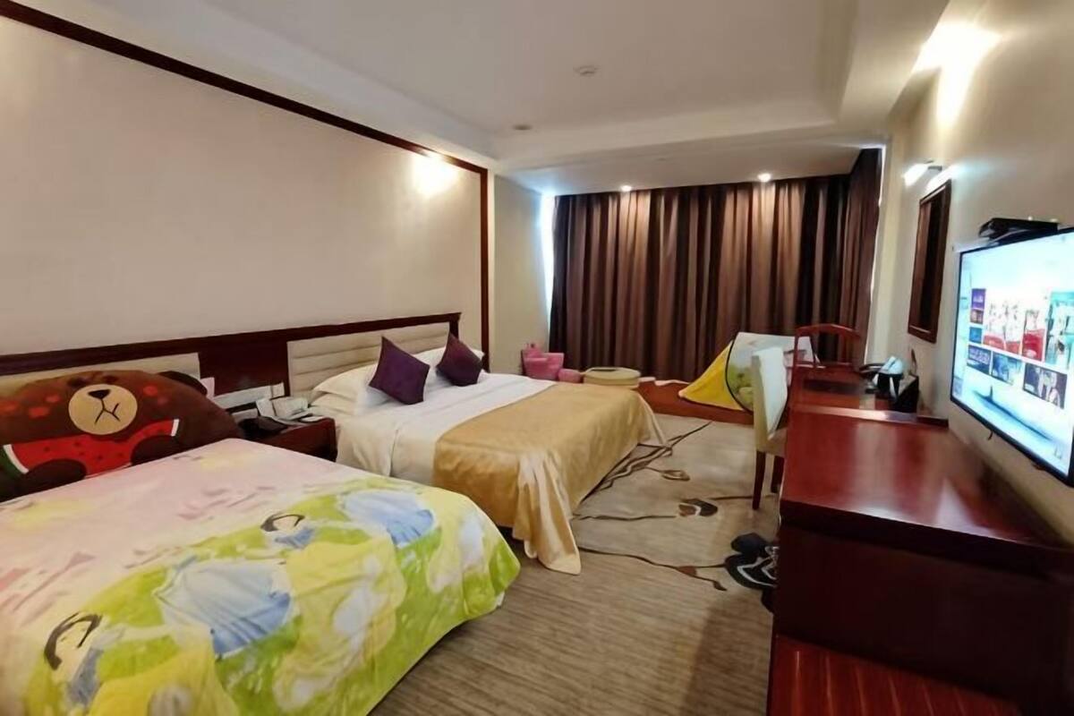 A hotel room with two beds, a TV, a desk, and a window with curtains.