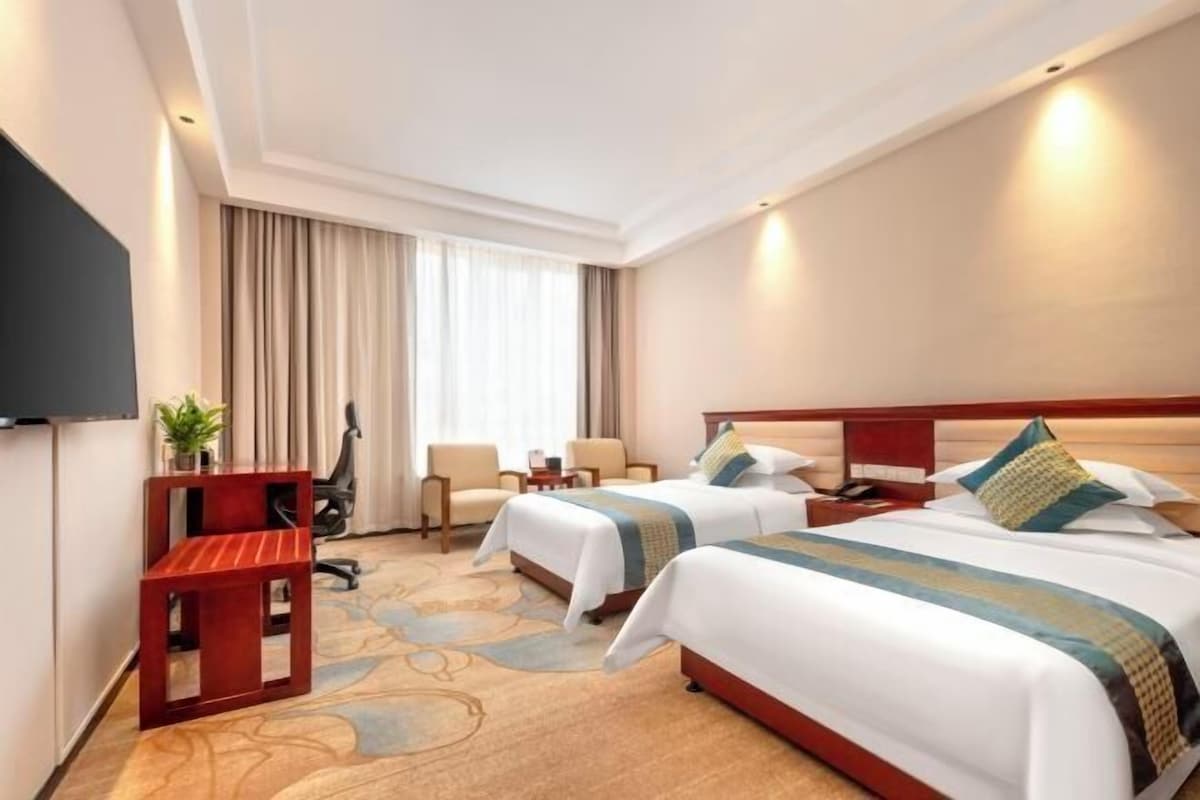 Quarto de hotel com duas camas, televisão, escrivaninha e cadeira.