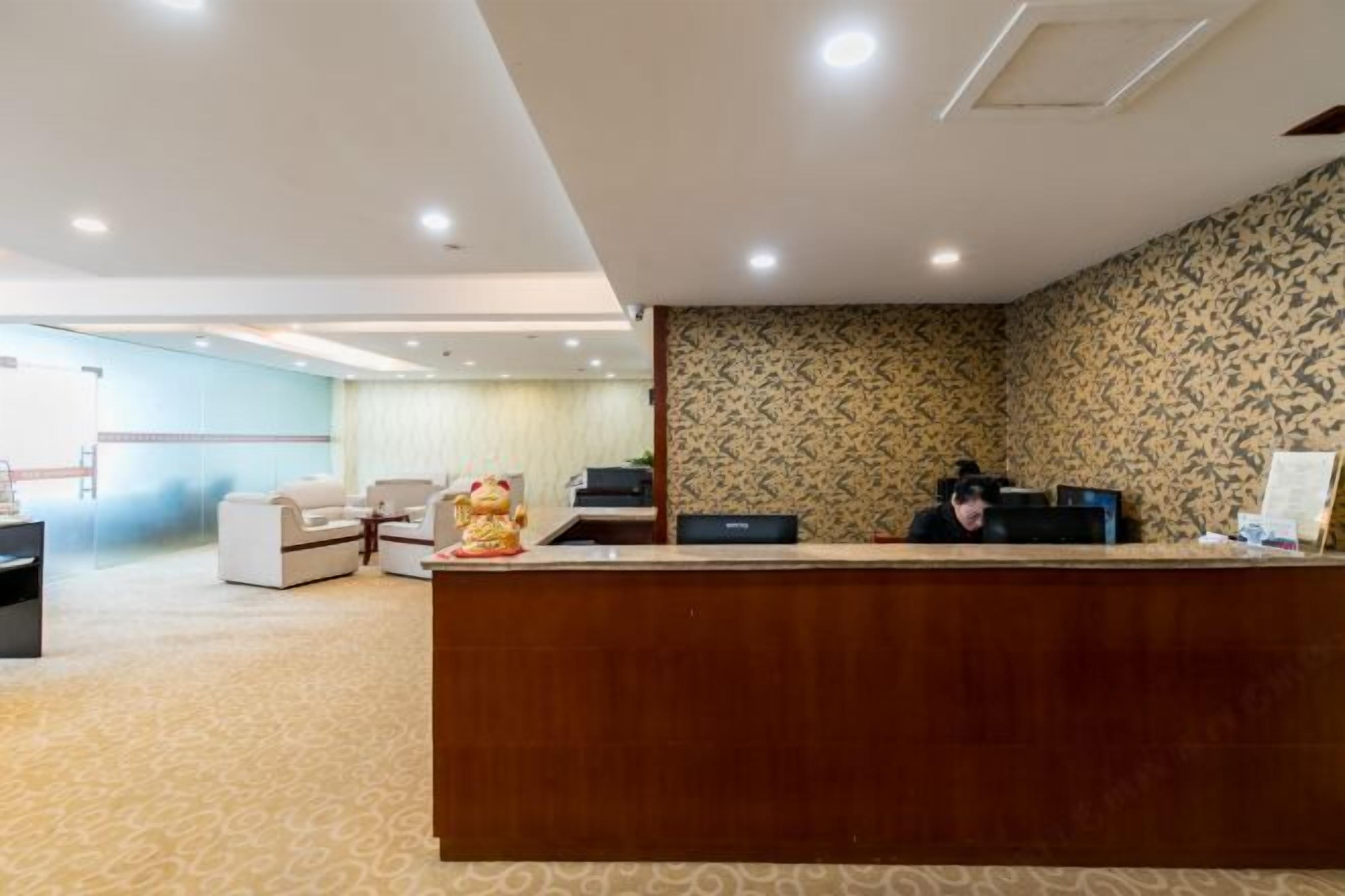 A reception area with a wooden desk, a receptionist, and a patterned wall.