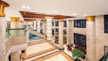 Un lobby amplio con columnas de mármol, una escalera central y una zona de estar con una planta.