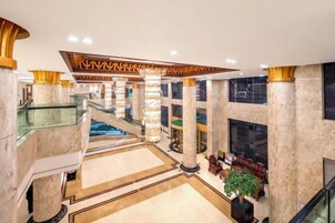 Un lobby amplio con columnas de mármol, una escalera central y una zona de estar con una planta.