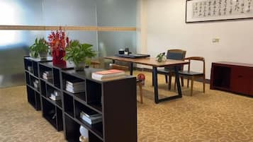 Una habitación con escritorio, sillas, una estantería y un arreglo decorativo de plantas.