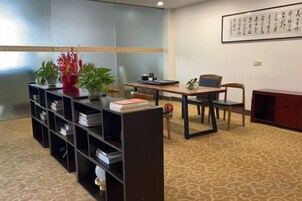 Una habitación con escritorio, sillas, una estantería y un arreglo decorativo de plantas.
