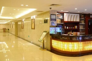 Zona de recepción de hotel con mostrador curvo, cuadros enmarcados en las paredes y un panel informativo digital.