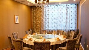Un salón de conferencias con una mesa redonda, sillas estampadas, una araña y un ventanal con cortinas decoradas.