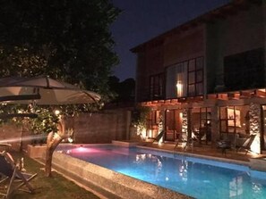 Una casa moderna de dos pisos con piscina, mobiliario exterior y un patio bien iluminado.