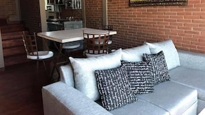 Un salon confortable avec un canapé, une table à manger et des chaises. On aperçoit une cuisine au fond.