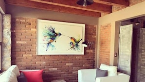 Un salon moderne avec un mur en briques, des canapés blancs et un tableau coloré représentant un oiseau.