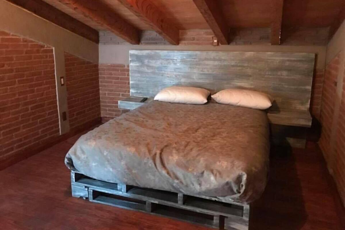 A bedroom with a wooden headboard, a bed with a blanket, and a brick wall.