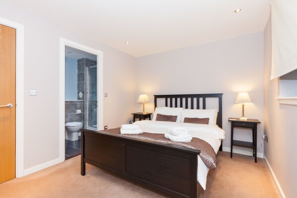 Une chambre à coucher comprenant un lit, des tables de chevet, une commode, une porte et une salle de bain avec des toilettes et une douche.