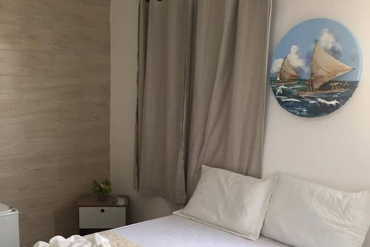 A hotel room with a bed, curtains, a nightstand, and a wall painting.