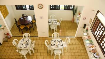 A dining area with two tables, one round and one square, both with white chairs. There is a clock on the wall and a fire extinguisher near the entrance.