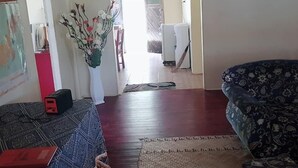 A living room with a patterned sofa, a small table with a red box, a decorative plant, and a view into the kitchen area. - Navutovuto Accommodation (Kadavu Island)