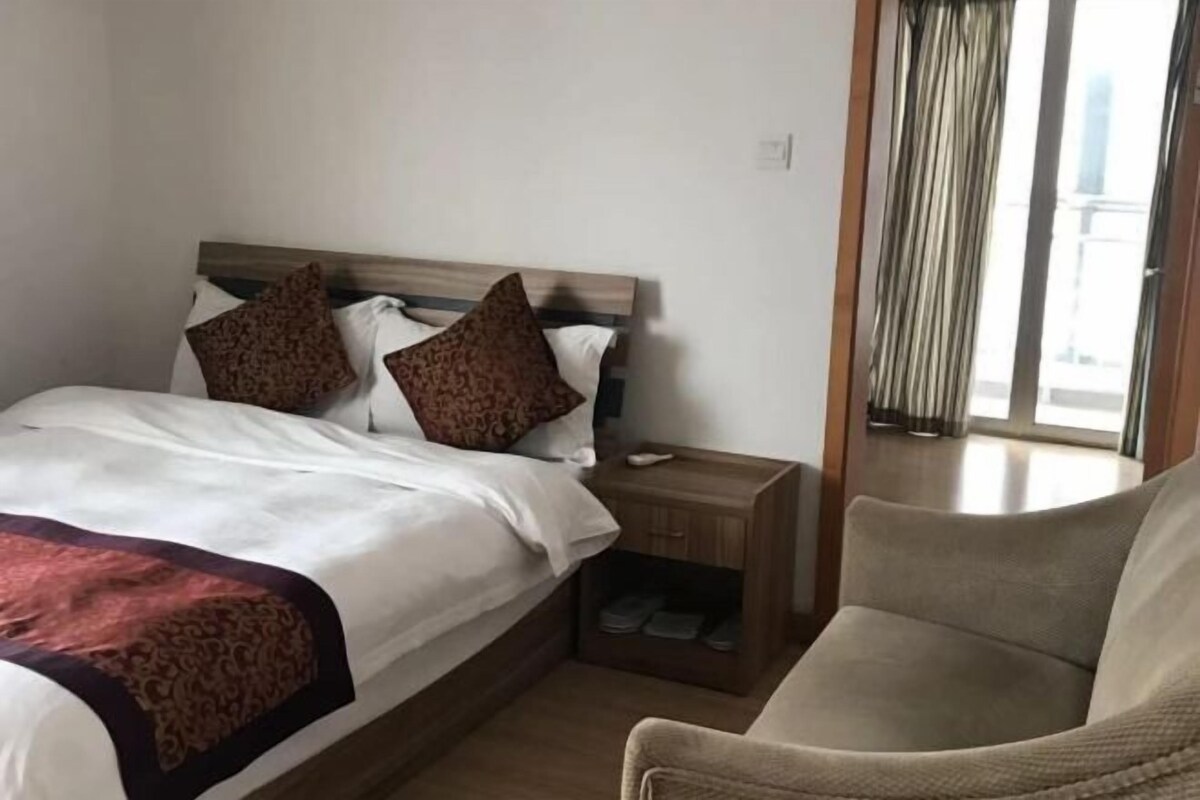 A hotel room with a bed, a nightstand, a chair, and a view of the outside.