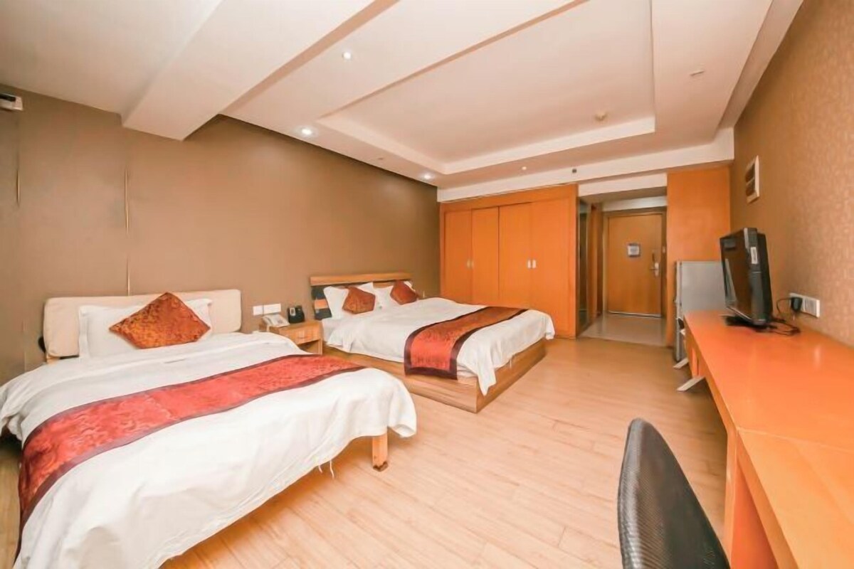 A hotel room with two beds, a desk, a chair, and a television.