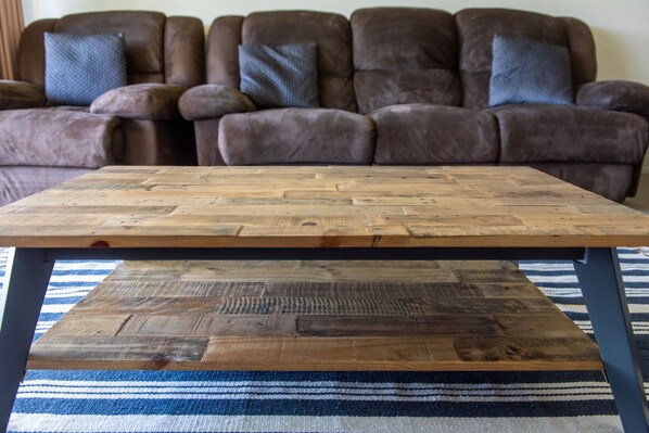 A wooden coffee table with a striped rug in front of a brown leather sofa.